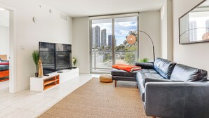 A modern living room with a large flat-screen TV, a dark leather sofa, a white entertainment unit, and a large window offering a city view. - Chic Miami Condo w/ Pool, 6 Mi to South Beach (Miami)