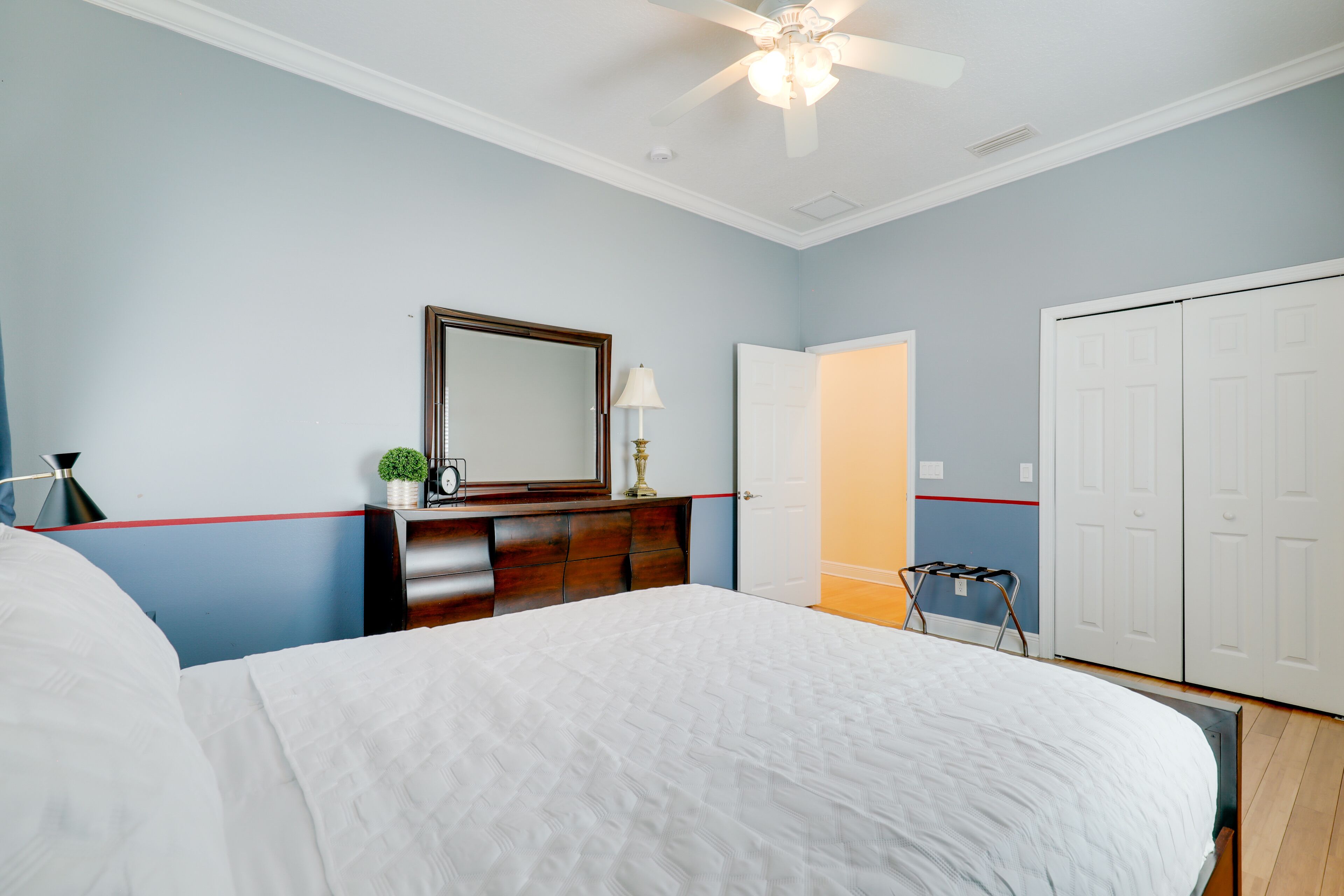 Une chambre à coucher comprenant un lit, une commode, un miroir, un ventilateur de plafond et une armoire.