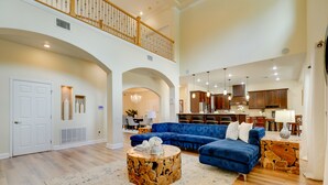 A spacious living room with a blue sectional sofa, a wooden coffee table, and a dining area with a chandelier. - Contemporary Brandon Home w/ Pool & Game Room (Brandon)