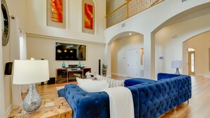 A spacious living room with a large blue sofa, a wooden coffee table, and a flat-screen TV mounted on the wall. - Contemporary Brandon Home w/ Pool & Game Room (Brandon)