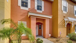 A two-story building with a red exterior and white trim. There are two visible windows with shutters, a porch with a white railing, and a small garden with palm trees. - Chic Florida Retreat ~ 7 Mi to Walt Disney World! (Kissimmee)
