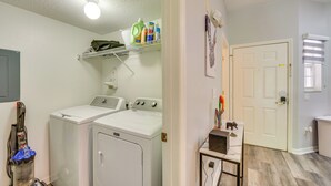 A laundry room with two white front-loading washers and dryers, a vacuum cleaner, and a shelf with cleaning supplies. - Chic Florida Retreat ~ 7 Mi to Walt Disney World! (Kissimmee)