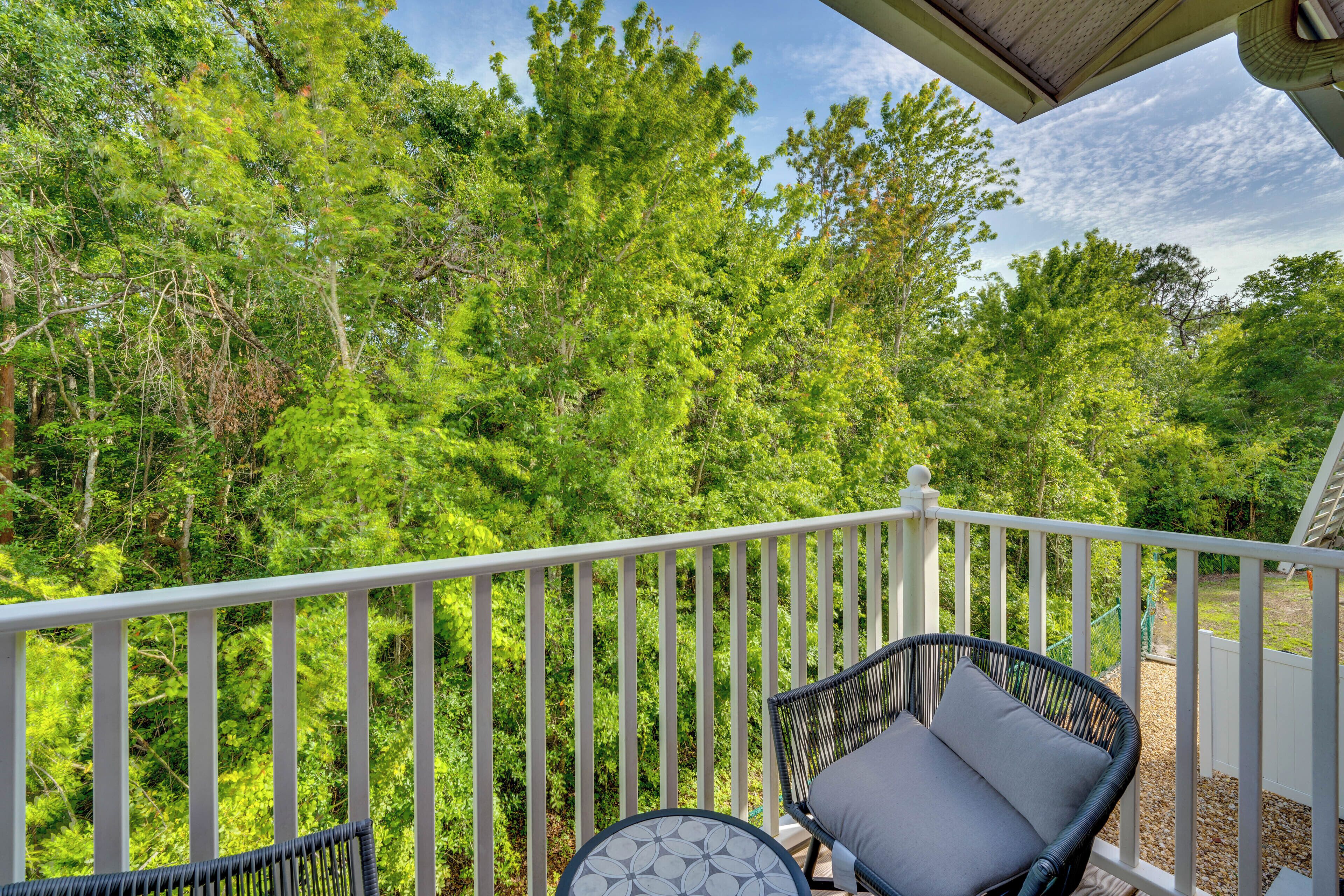 A balcony with white railings, a wicker chair with a cushion, and a round table with a patterned top.