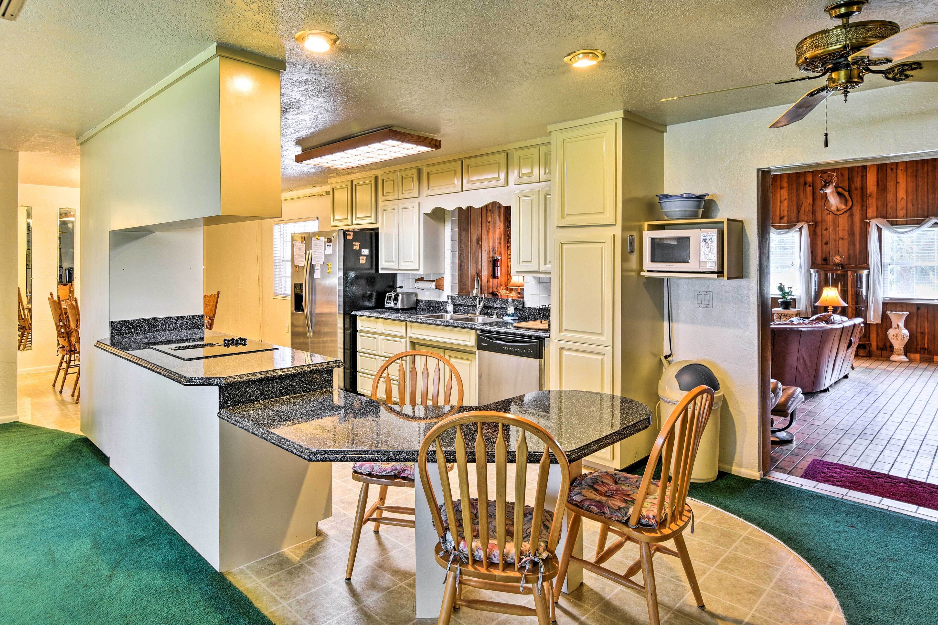 A compact kitchen with a central island, wooden chairs, and a ceiling fan.