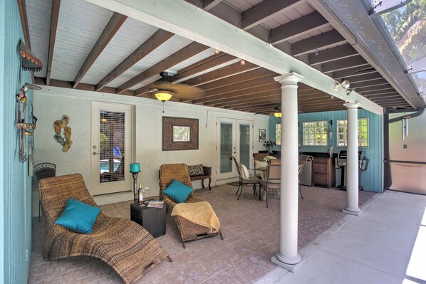 Un patio techado con mobiliario de mimbre, una mesa de comedor y una zona de cocina.