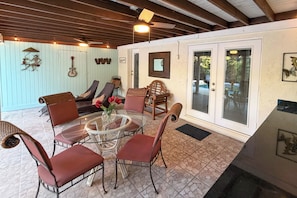 A covered patio area with a glass table surrounded by chairs, a sofa, and a decorative wall with mounted items.