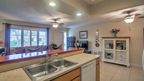 Una cocina moderna con lavavajillas, pileta doble y un comedor con televisor y libros.