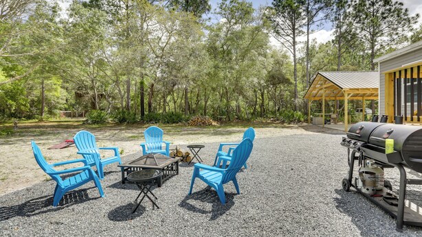 An outdoor seating area with blue Adirondack chairs, a fire pit, and a grill.