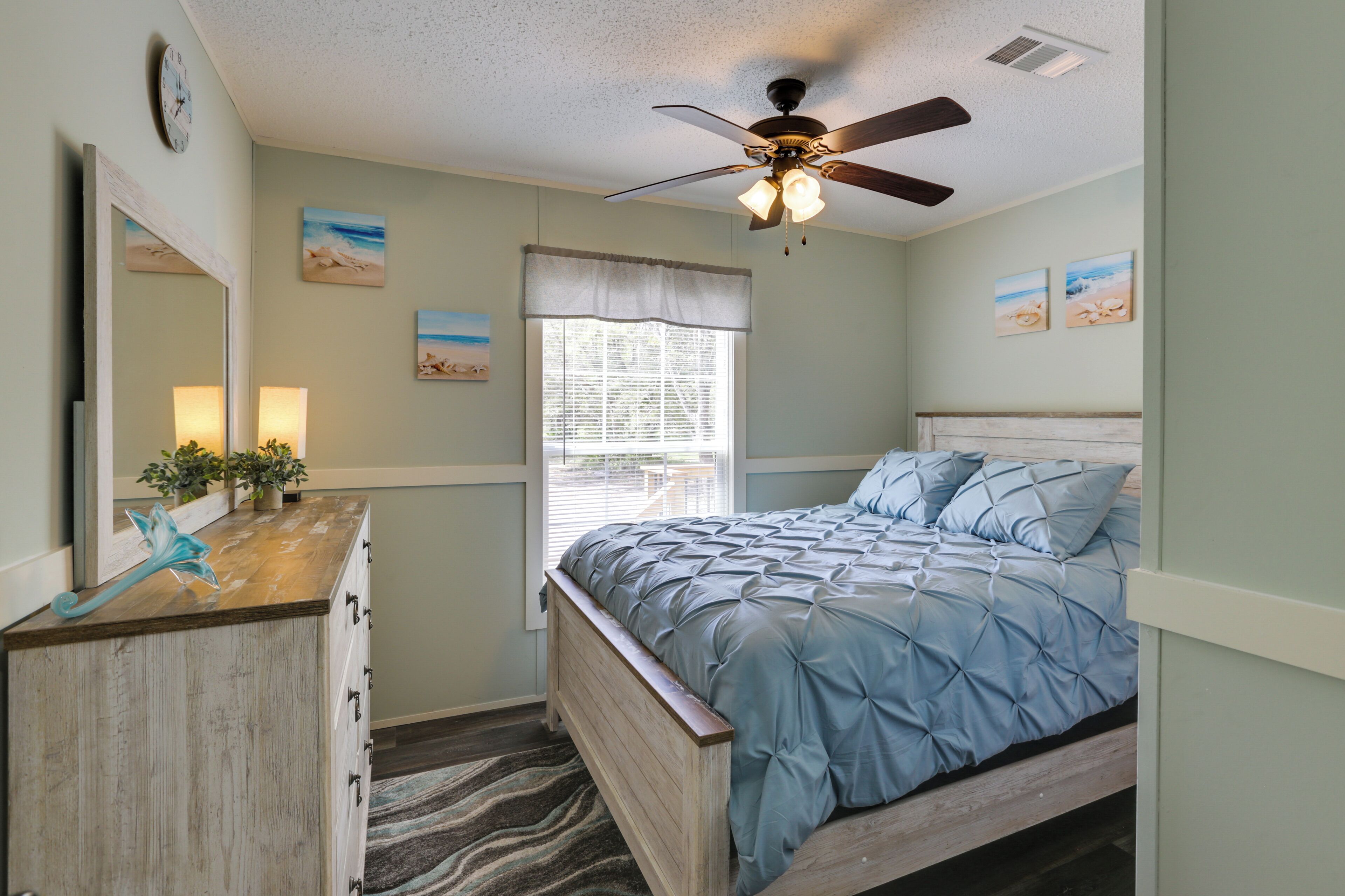 A bedroom with a bed, a dresser, a ceiling fan, and artwork on the walls.
