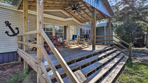 Una terraza de madera con una escalera que conduce a un porche cubierto con mobiliario exterior.
