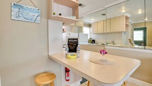 A kitchen with a curved island, wooden stools, a welcome sign, and a small plant. - Cozy Ormond Beach Bungalow: Steps to the Sand (Ormond Beach)