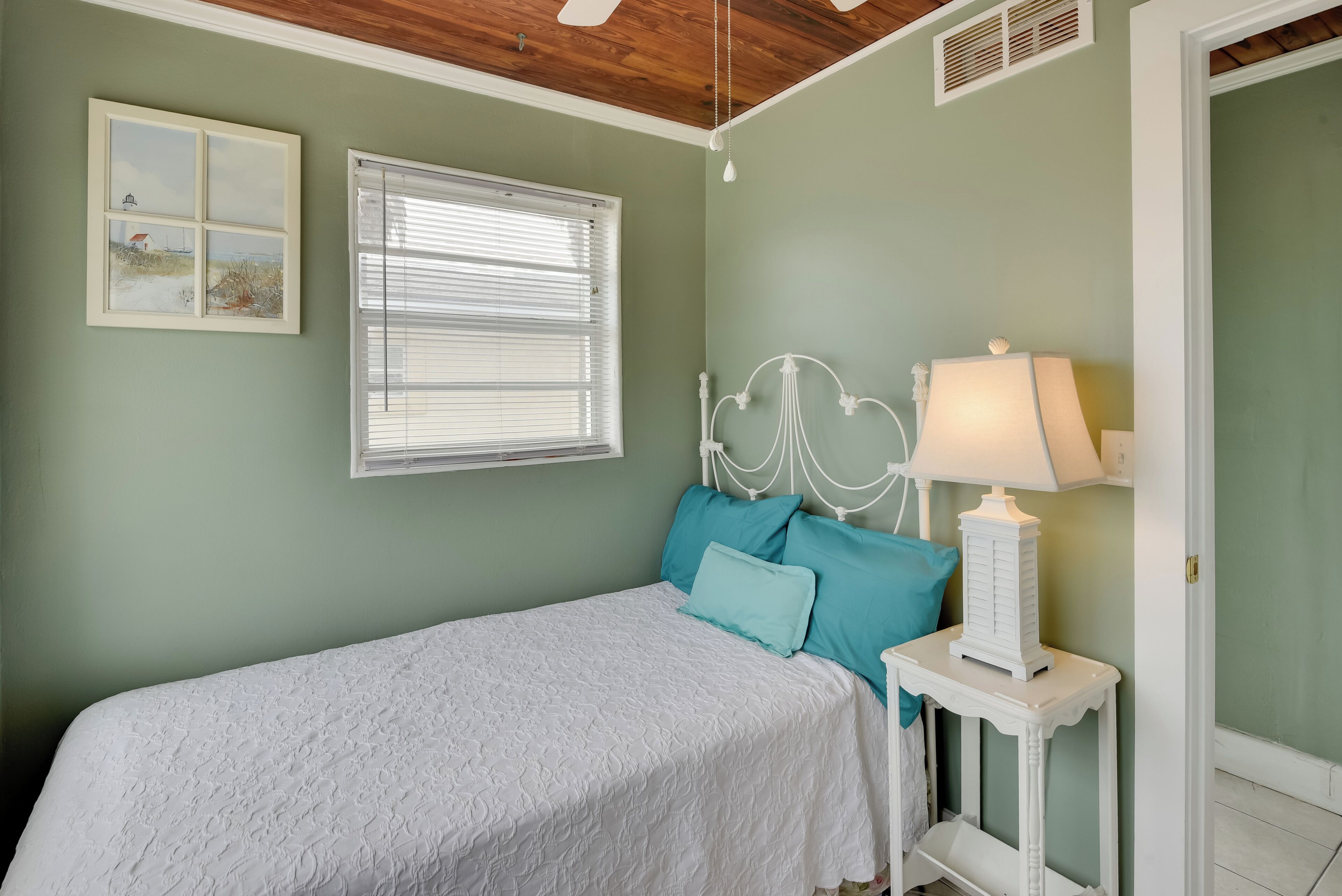 A bedroom with a bed, a nightstand, a lamp, a window with blinds, and a wall with a picture.