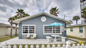 A two-story house with a white picket fence, a patio with outdoor furniture, and palm trees. - Cozy Ormond Beach Bungalow: Steps to the Sand (Ormond Beach)