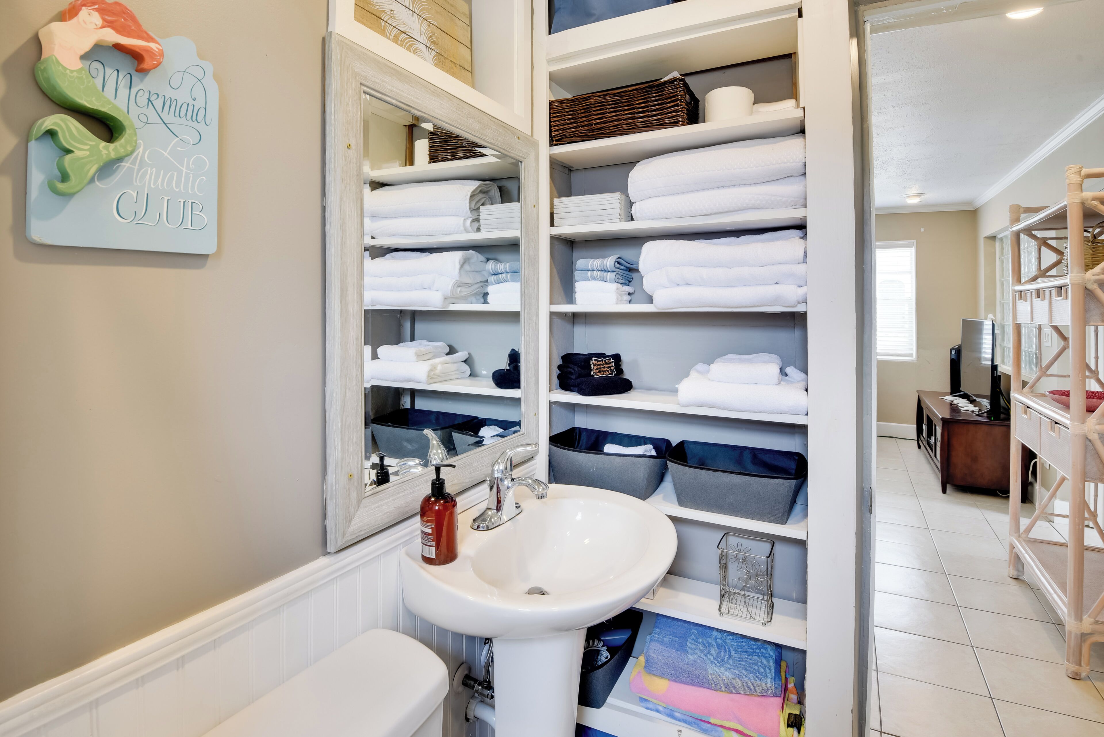 Une salle de bain avec un lavabo blanc, un miroir et des étagères où sont soigneusement pliées des serviettes.