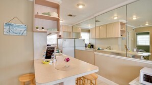 A modern kitchen with a central island, wooden stools, and a large mirror. - Cozy Ormond Beach Bungalow: Steps to the Sand (Ormond Beach)