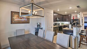 A modern kitchen with dark cabinetry, a central island, and a dining area with a dark wooden table and grey upholstered chairs. - Charming Poinciana House w/ Patio: 30 Mi to Disney (Kissimmee)