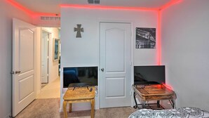 A room with a white door, a television on a wooden stand, and a cross on the wall. - Charming Poinciana House w/ Patio: 30 Mi to Disney (Kissimmee)