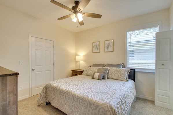 A bedroom with a bed, a ceiling fan, a nightstand, a lamp, and two framed pictures on the wall.