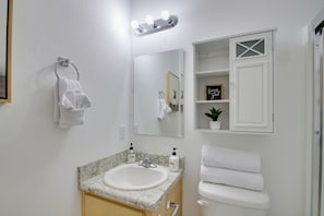 Un baño con lavamanos de mármol, sanitarios blancos, tocador y espejo con luces.