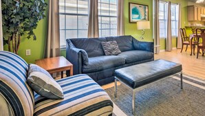 A living room with a dark blue sofa, striped armchair, and ottoman, a wooden coffee table, and a large green plant. - Cute Pensacola Townhome ~ 9 Mi to Downtown! (Pensacola)
