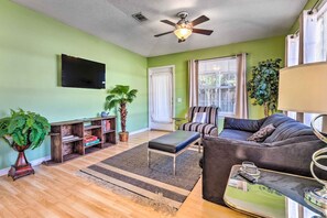 Ein Wohnzimmer mit einer Couch, einem Couchtisch, einem an der Wand befestigten Fernseher, einem Deckenventilator und einer großen Pflanze.