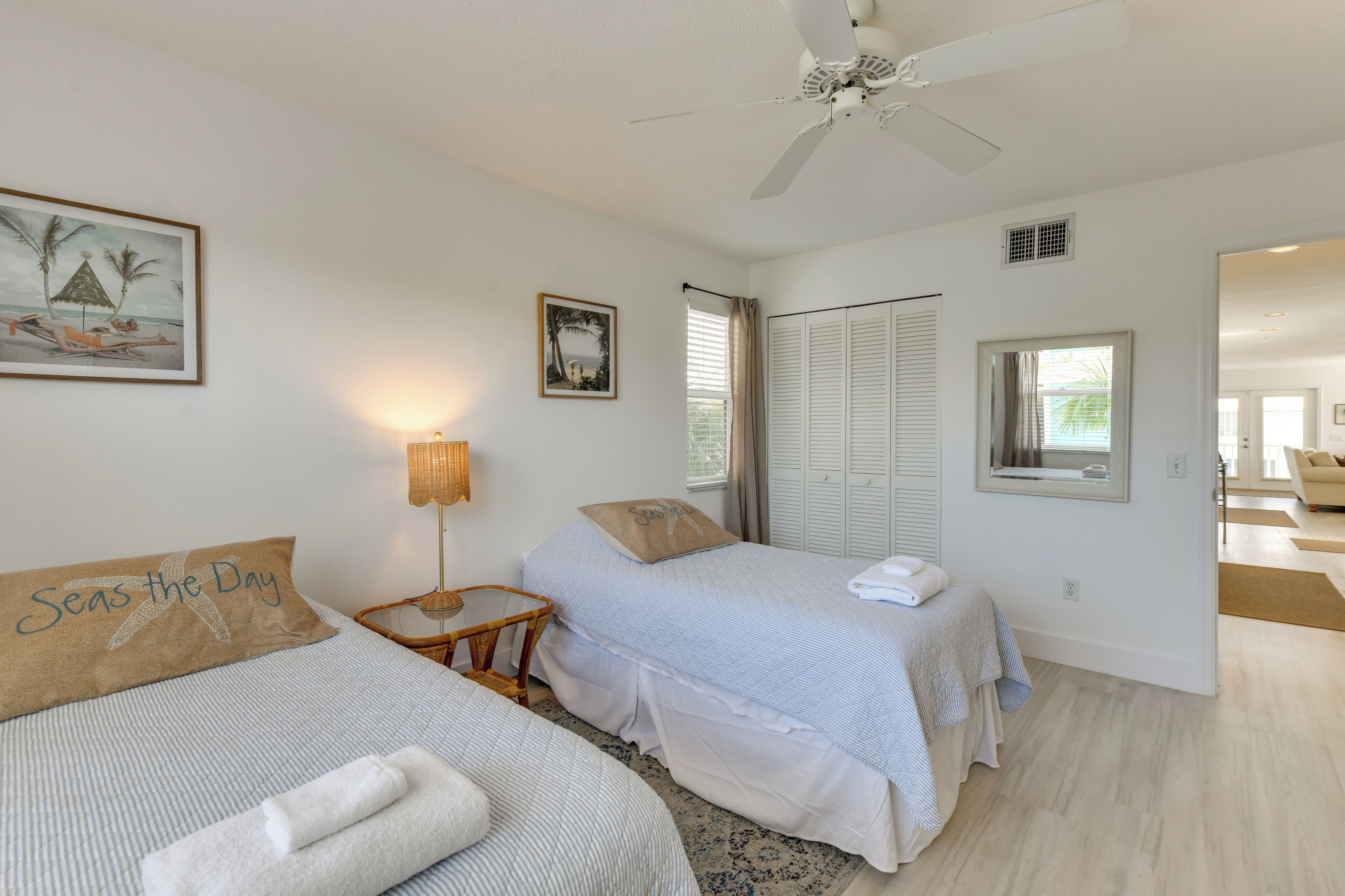 Une chambre avec deux lits, un ventilateur de plafond, une fenêtre avec des rideaux et une porte donnant sur une autre pièce.