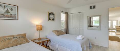 Une chambre avec deux lits, un ventilateur de plafond, une fenêtre avec des rideaux et une porte donnant sur une autre pièce.