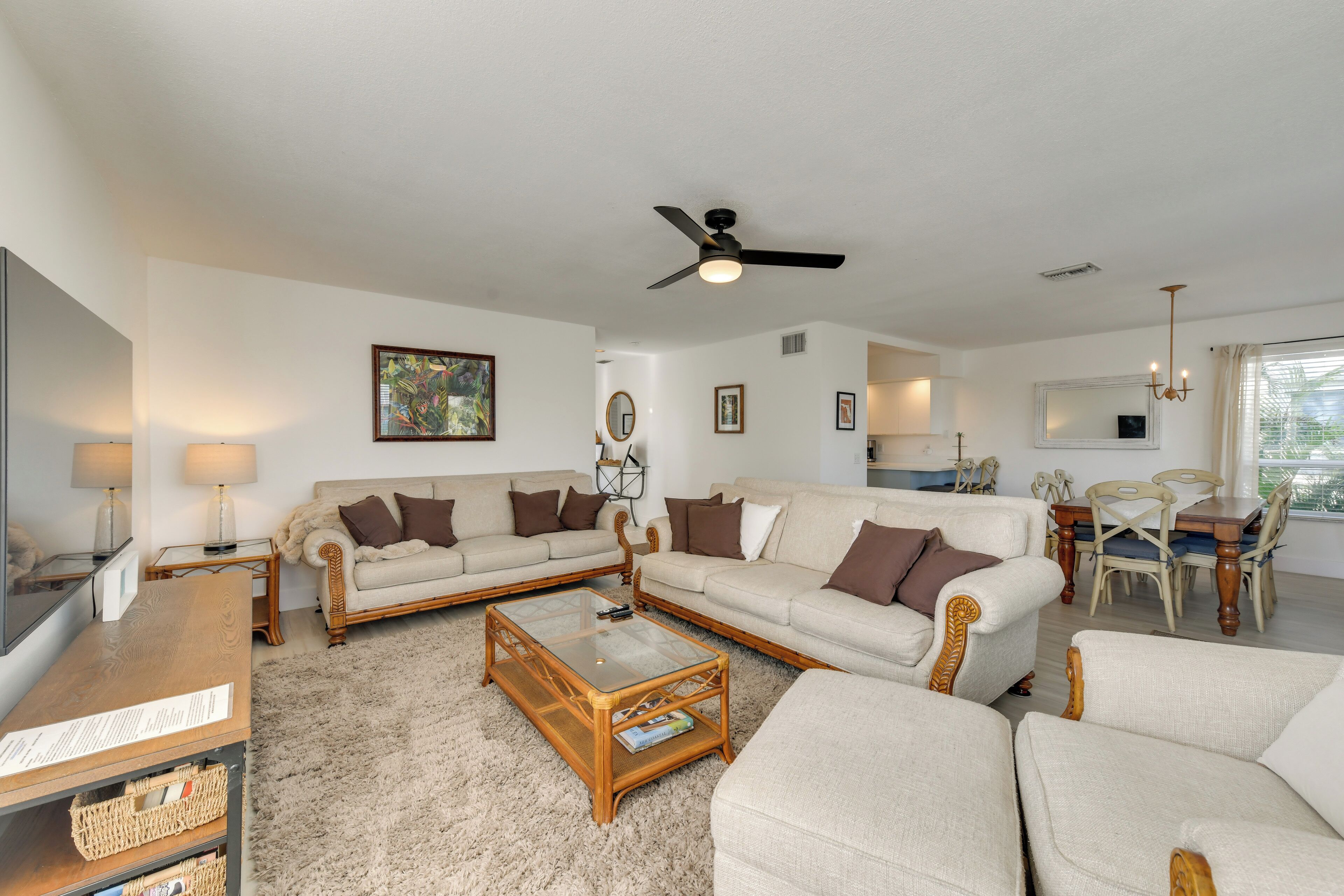 A spacious living room with a large flat-screen TV, two sofas, a coffee table, and a dining area with a wooden table and chairs.