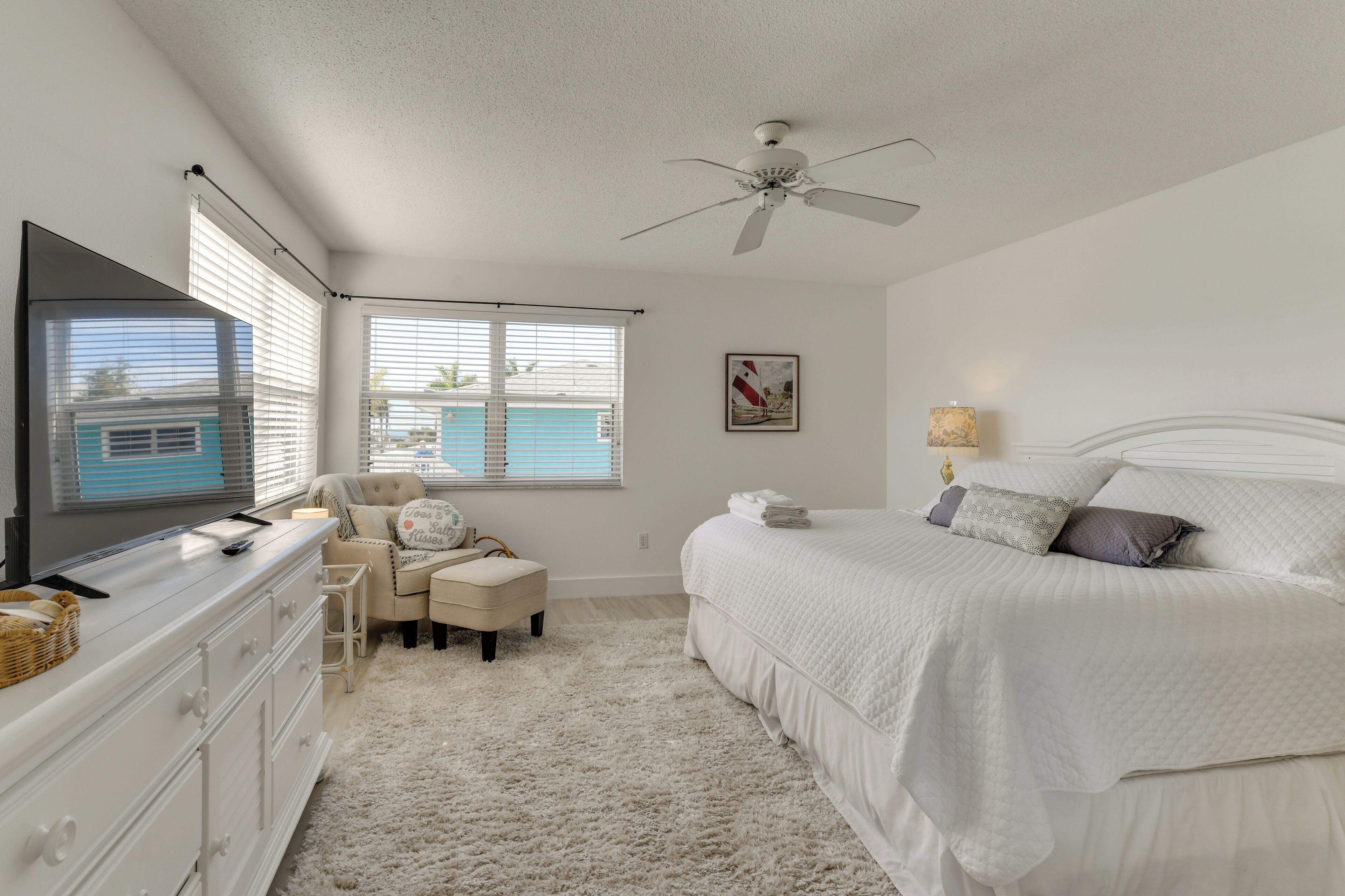 A bedroom with a bed, a dresser, a chair, a desk, a ceiling fan, and a window with blinds.