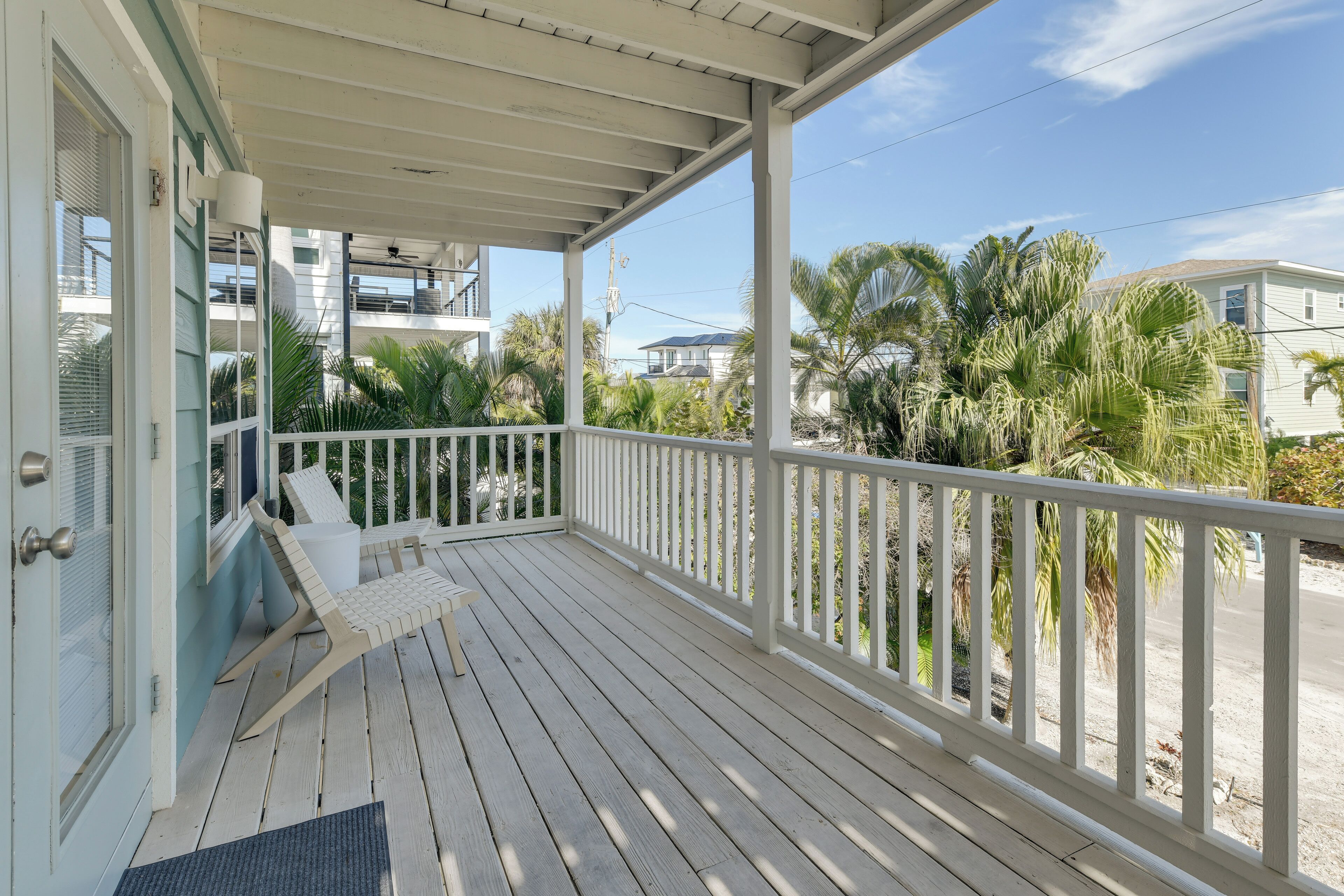 A wooden deck with a white railing, a bench, and a door.