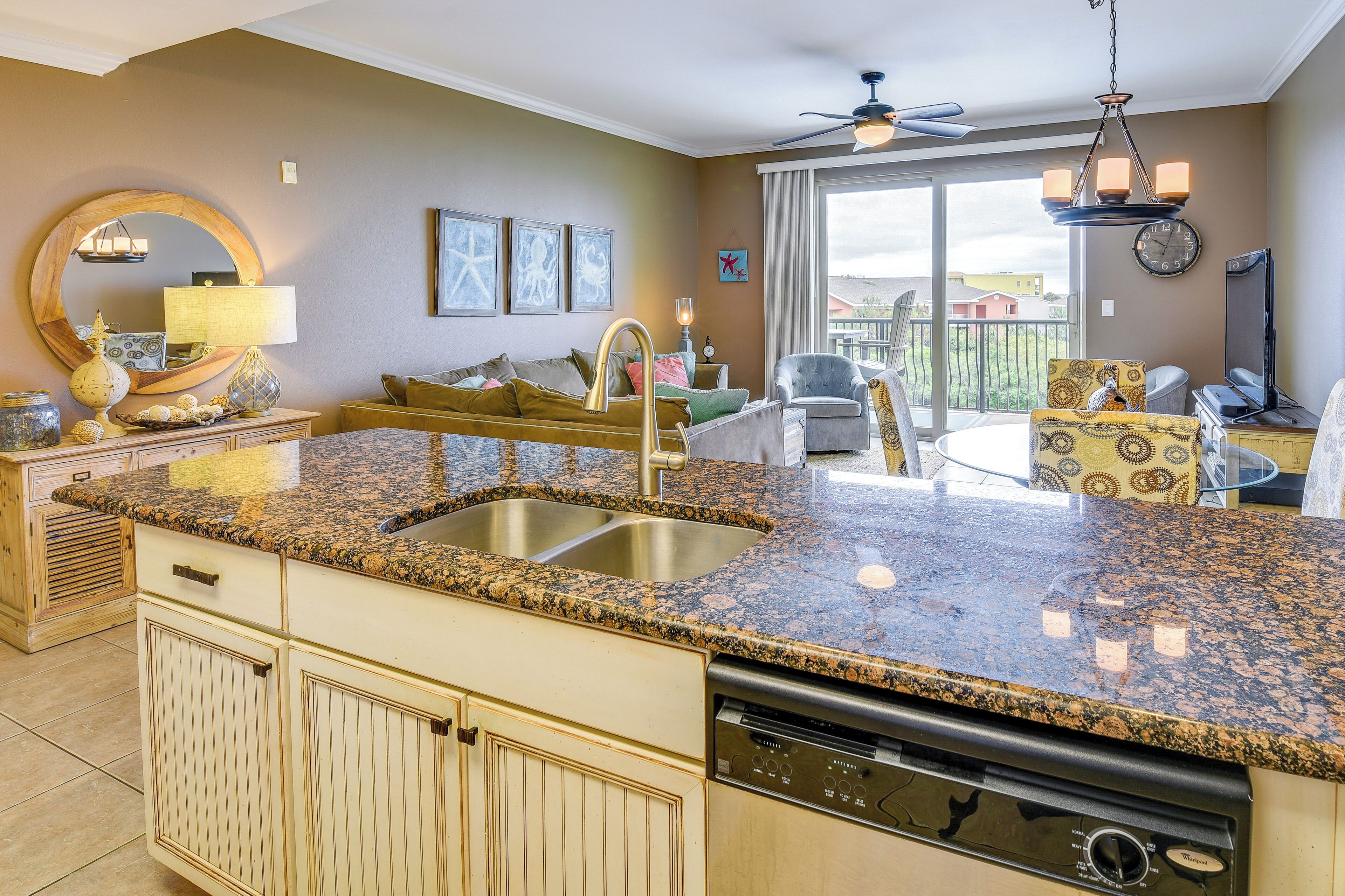 A kitchen with granite countertops, a dishwasher, and a large window overlooking a balcony.