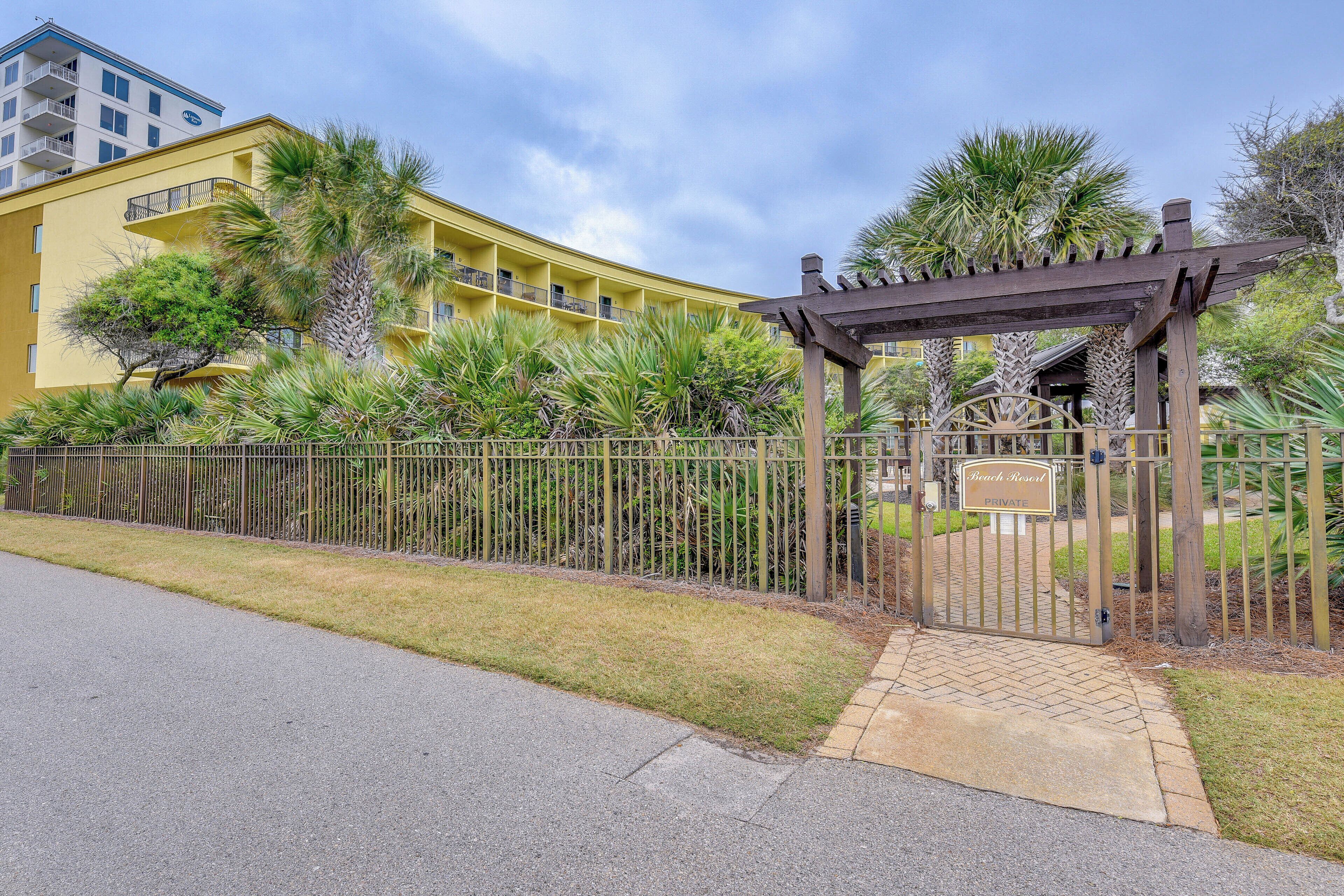 A gated entrance to a resort with a pergola and palm trees.