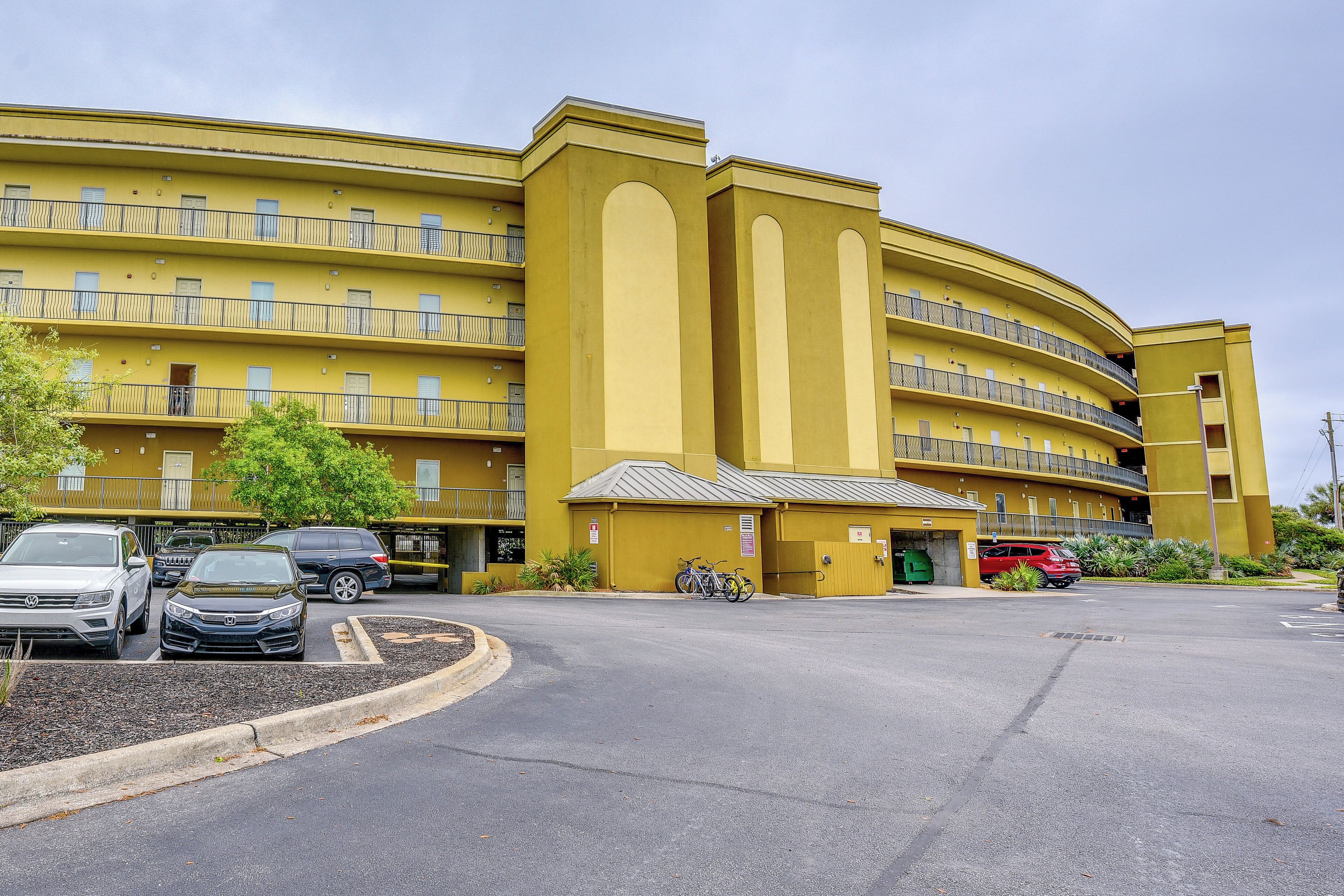 A multi-story yellow building with balconies, a parking lot, and several parked cars.