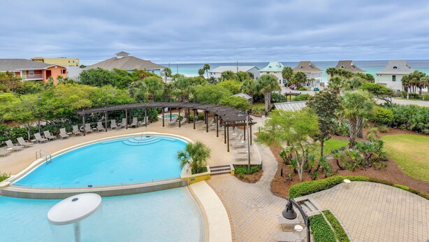 A swimming pool with lounge chairs and a gazebo, surrounded by greenery and houses with a view of the ocean. - Cozy Miramar Beach Condo w/ Pools & Beach Access! (Miramar Beach)