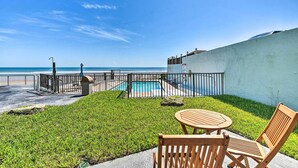 A pool area with a view of the ocean, a small lawn, and a wooden table and chairs. - Daytona Beach Retreat w/ Views & Pool Access! (Daytona Beach)