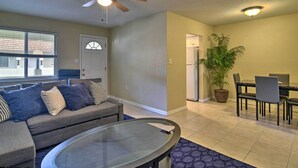 A living room with a gray sofa, a glass coffee table, a ceiling fan, a dining area with a table and chairs, and a potted plant. - Cozy Indian Rocks Beach Condo - Steps to Beach! (Indian Rocks Beach)
