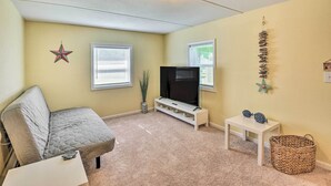 A cozy living room with a gray sofa, a flat-screen TV on a white stand, a small white table, and a woven basket. - Daytona Beach Home ~ 4 Mi to Daytona Speedway (Daytona Beach)