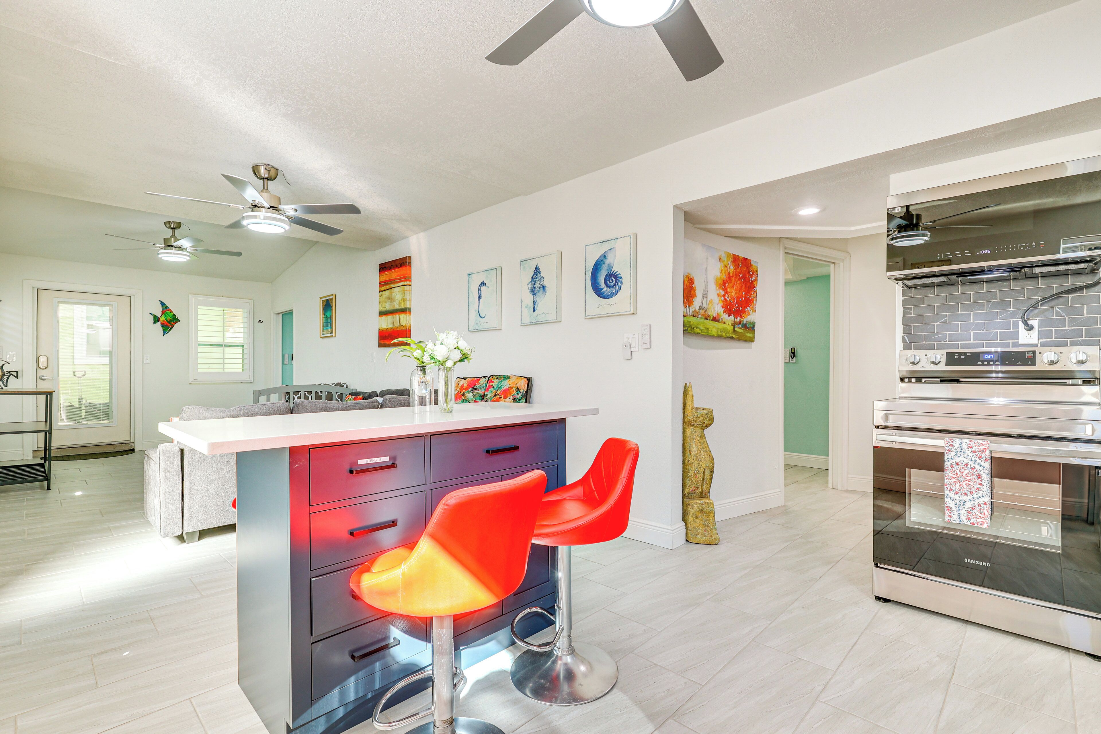 A modern kitchen with a central island, red bar stools, and a stainless steel oven.