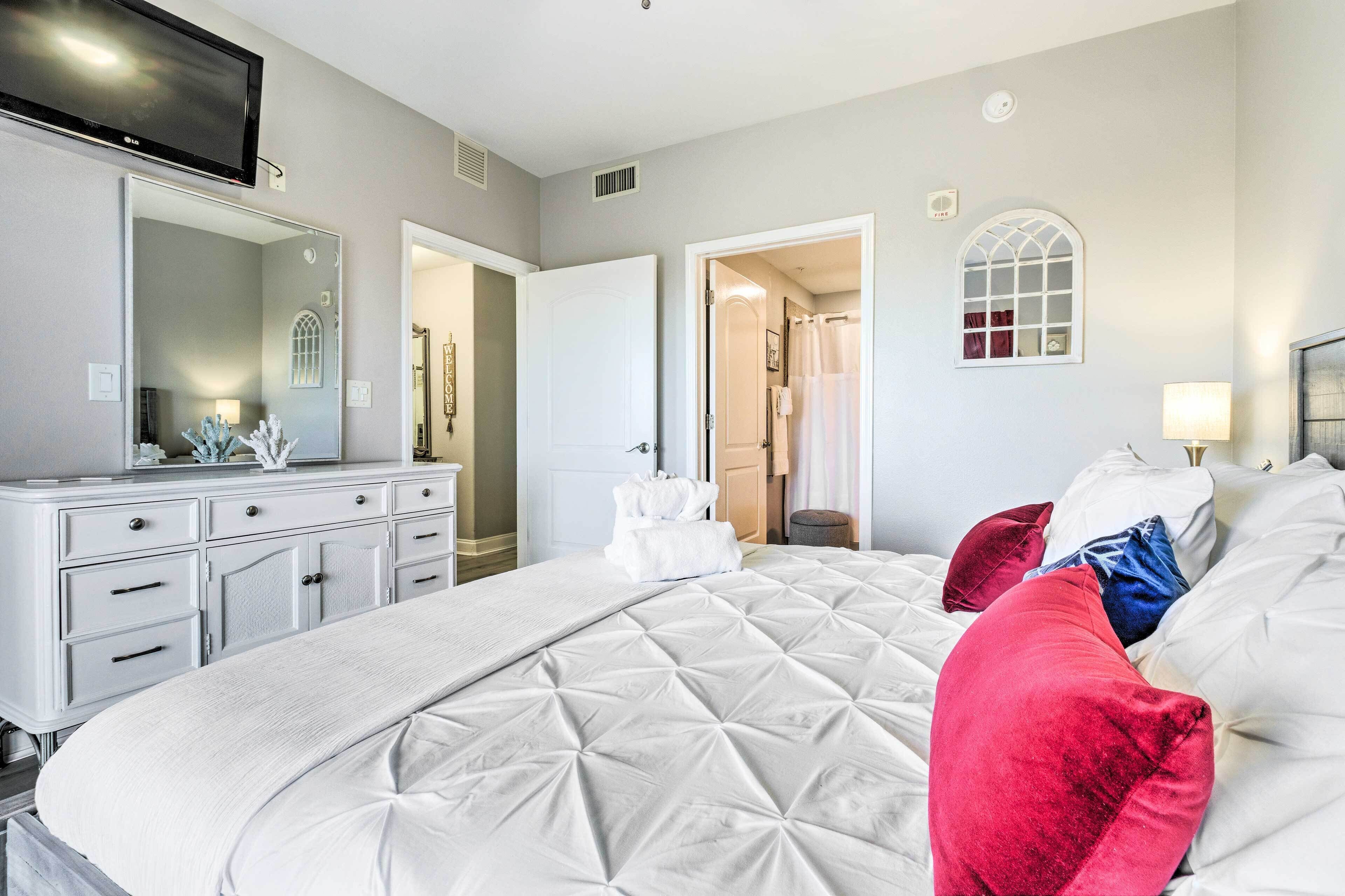 Une chambre d’hôtel avec un grand lit, une commode, un téléviseur et une salle de bain visible à travers une porte ouverte.