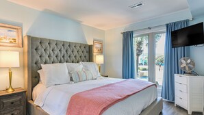 A bedroom with a large bed, a television mounted on the wall, a bedside table with a lamp, and a view of the outdoors through a window.