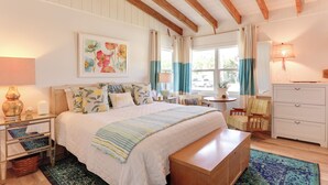 A bedroom with a large bed, a wooden bench, a nightstand, a lamp, a chair, a desk, and a dresser.