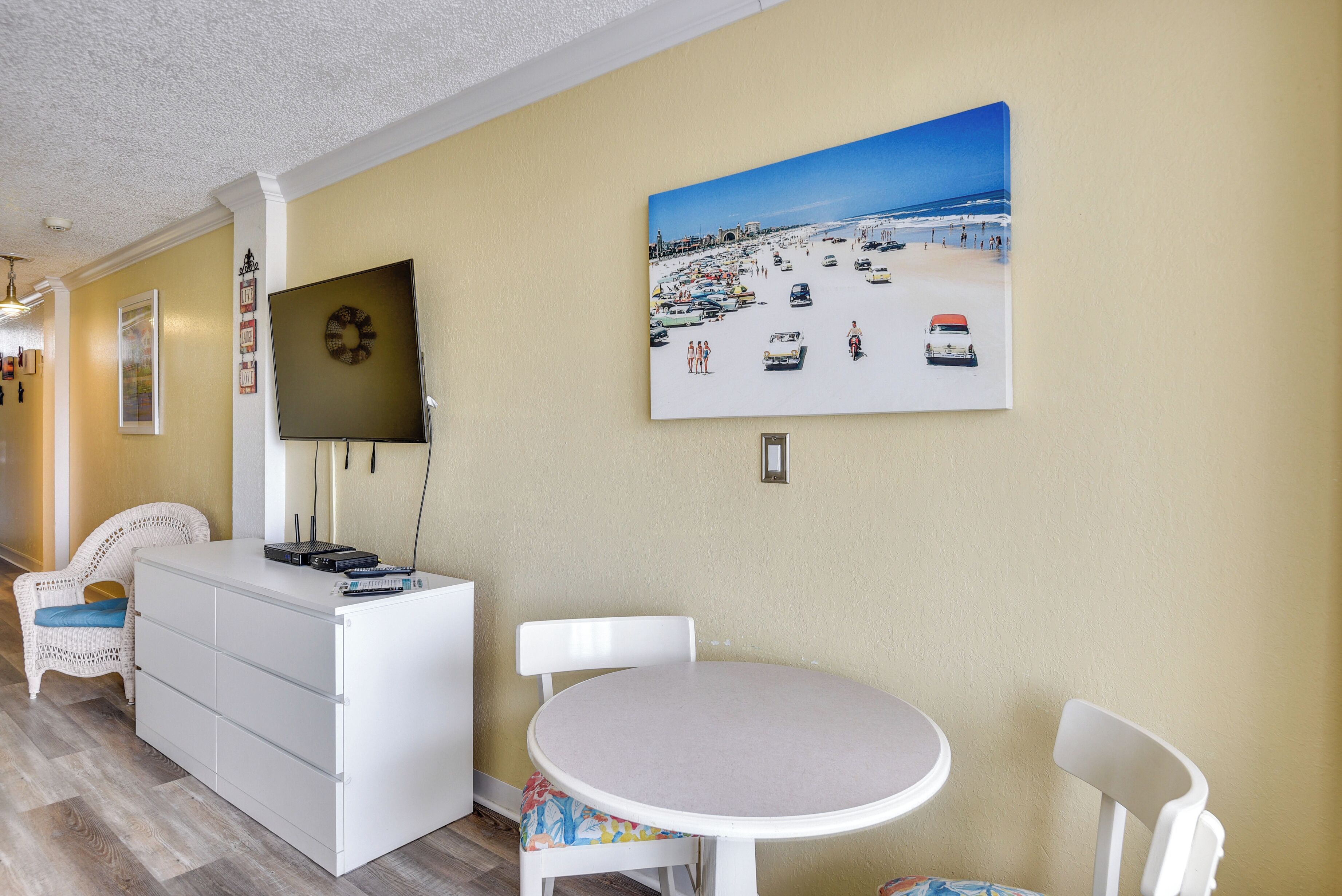Ein Zimmer mit weißem Schminktisch, einem runden Tisch und einem Wandbild zum Thema Strand.
