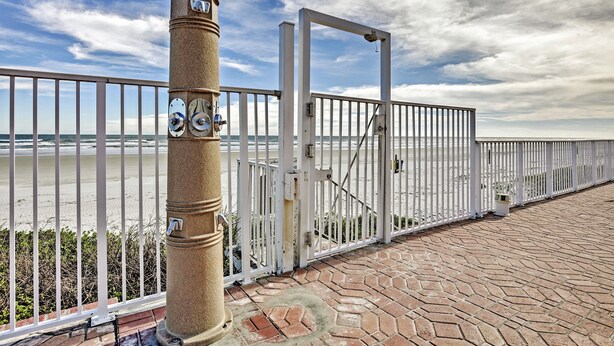 A coastal walkway with a metal fence, a gate, and a stone pillar. - Daytona Beach Studio w/ Private Lanai 1 Mi to Pier (Daytona Beach)
