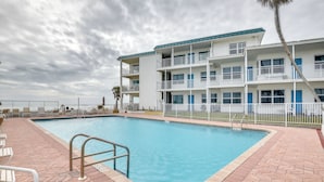 A swimming pool with a brick deck, white railings, and a multi-story building with balconies in the background. - Daytona Beach Studio w/ Private Lanai 1 Mi to Pier (Daytona Beach)