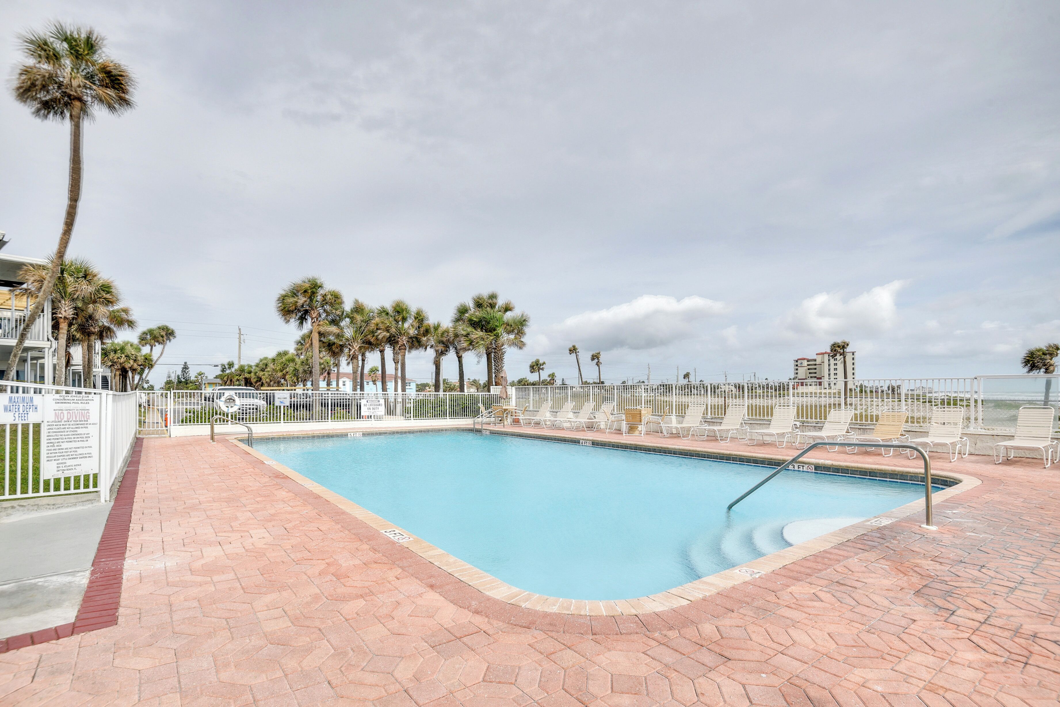 A swimming pool with a brick deck, surrounded by palm trees and a white fence.