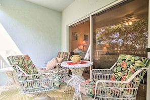 A patio with white wicker chairs and a table, a sliding glass door leading to a balcony, and a lamp on the table. - Idyllic Apt w/ Pool Access - Walk to Beach! (Lauderdale-by-the-Sea)