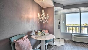 A room with a round table, two chairs, a chandelier, a large window with a view, and a wall-mounted air conditioner.