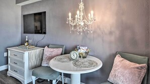 A room with a chandelier, a table with a clock, a dresser, and a chair.