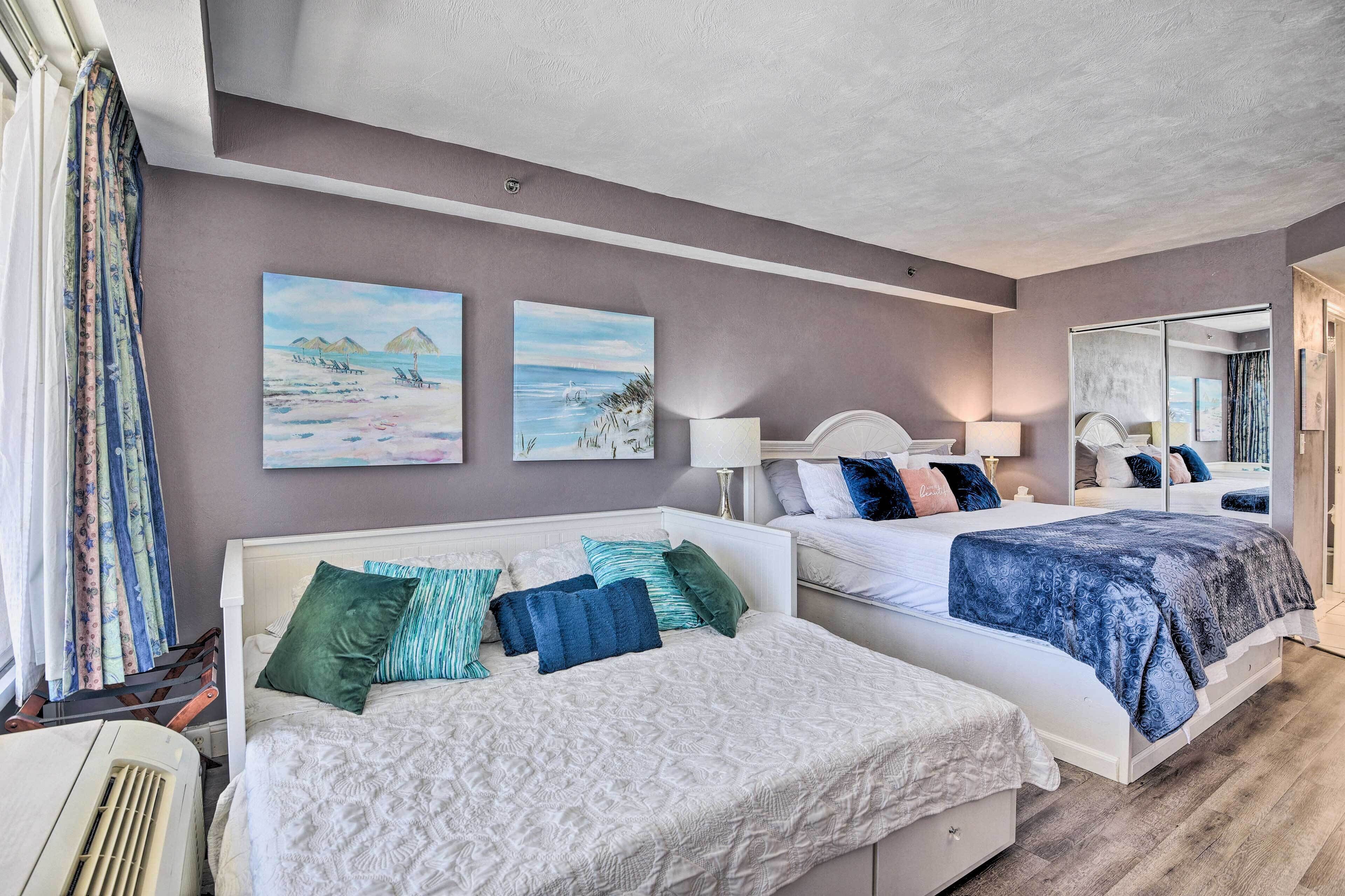 A hotel room with two beds, a large mirror, and beach-themed artwork on the walls.
