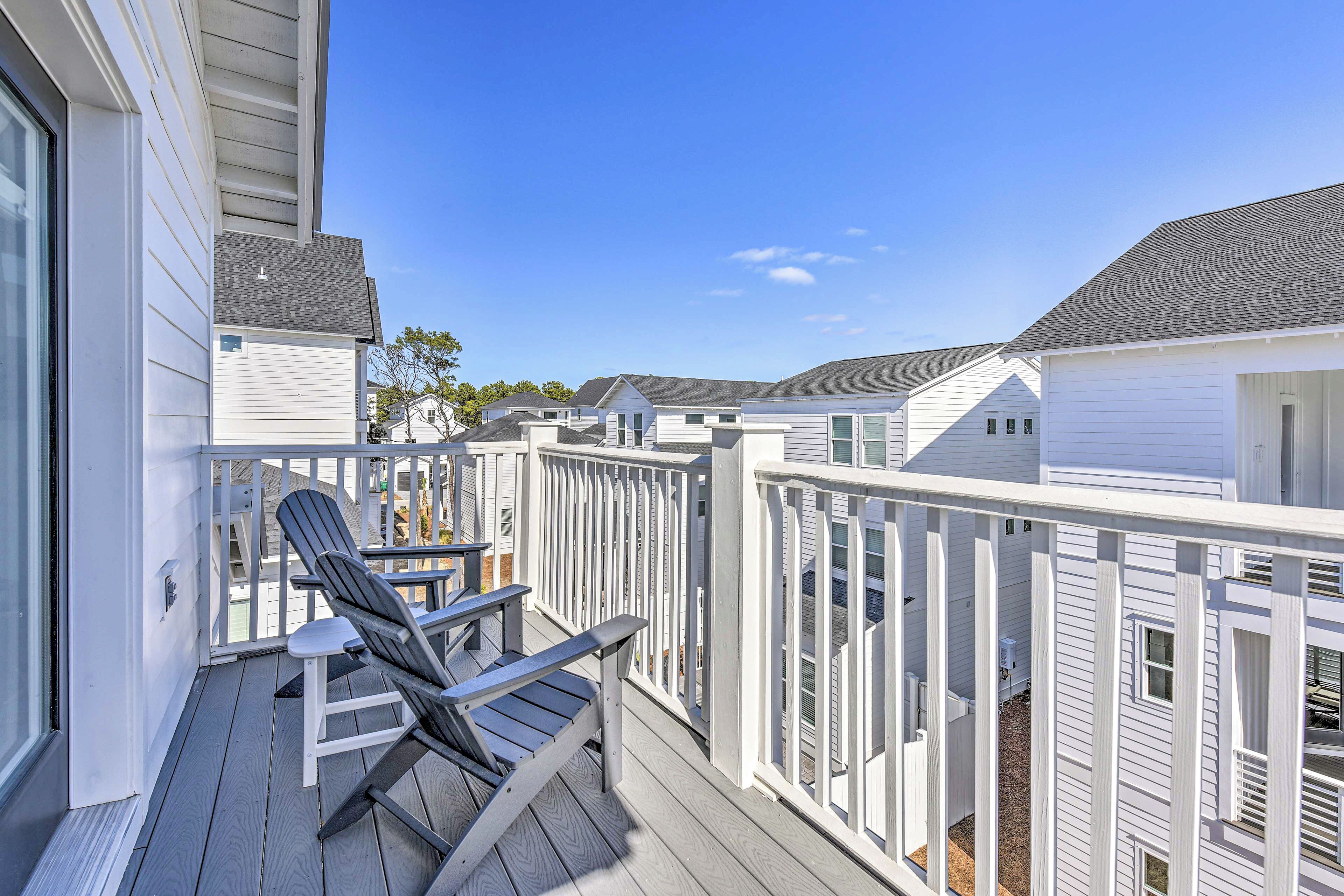 A wooden deck with two Adirondack chairs and a small table, surrounded by white railings and a clear blue sky.